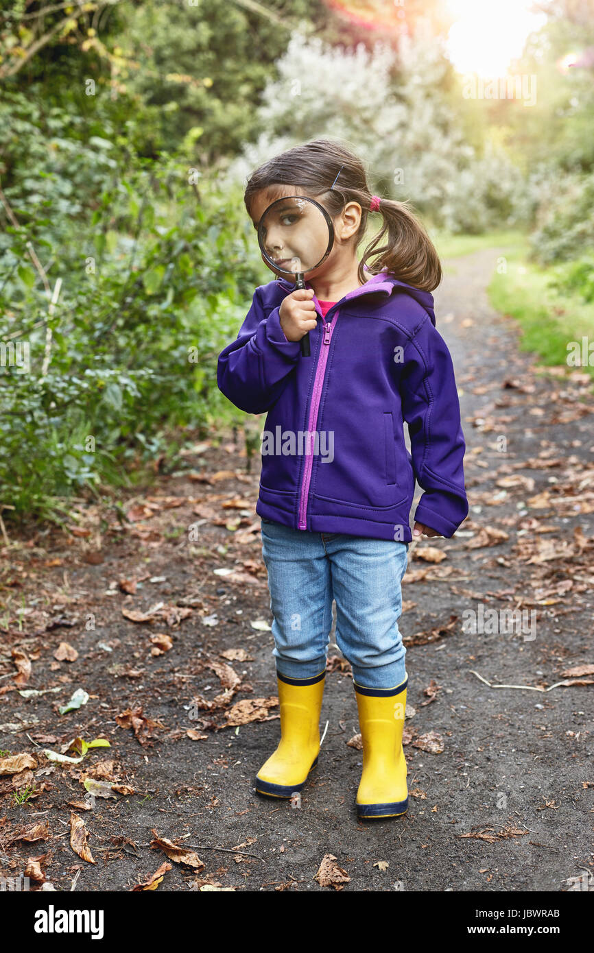 Ritratto di giovane ragazza sul percorso rurale, guardando attraverso la lente di ingrandimento Foto Stock