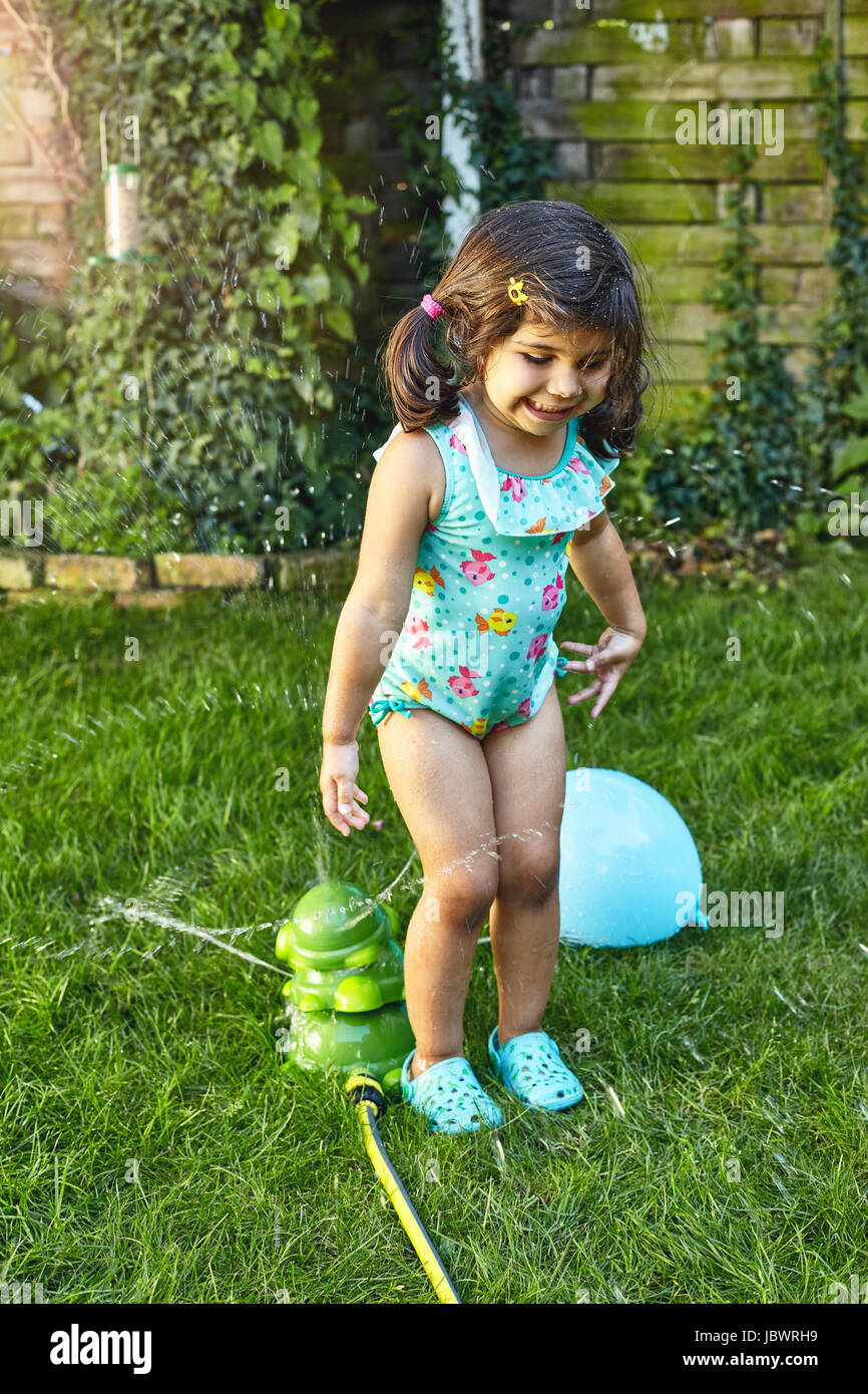 Ragazza giovane giocare in giardino, accanto all'acqua degli sprinkler Foto Stock