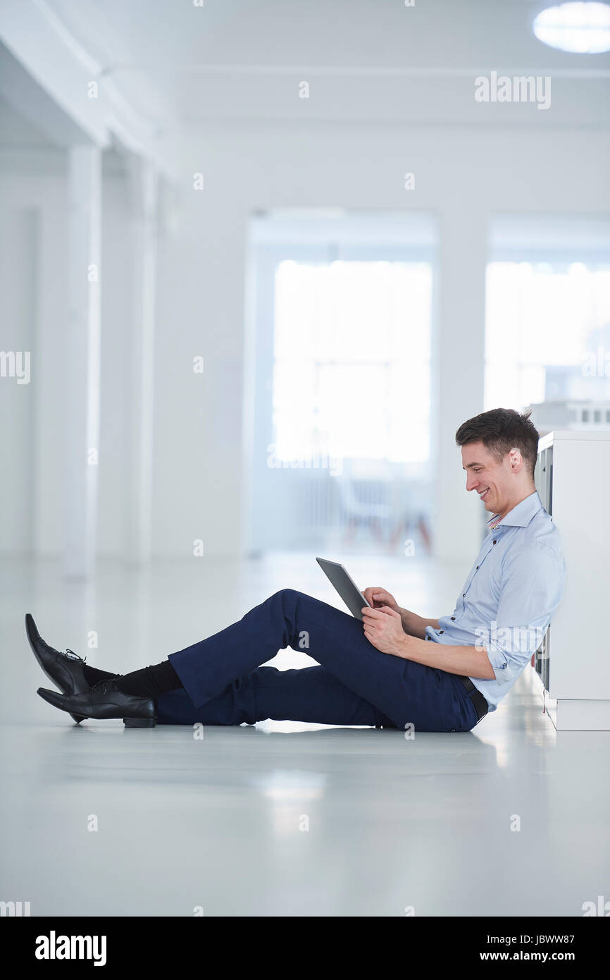 Uomo in ufficio seduti sul pavimento con tavoletta digitale Foto Stock