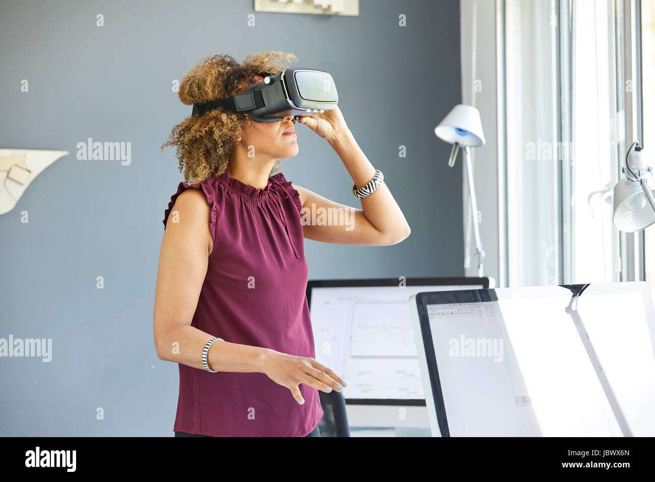 Architetto femmina cerca attraverso la realtà virtuale auricolare a scrivania da ufficio Foto Stock