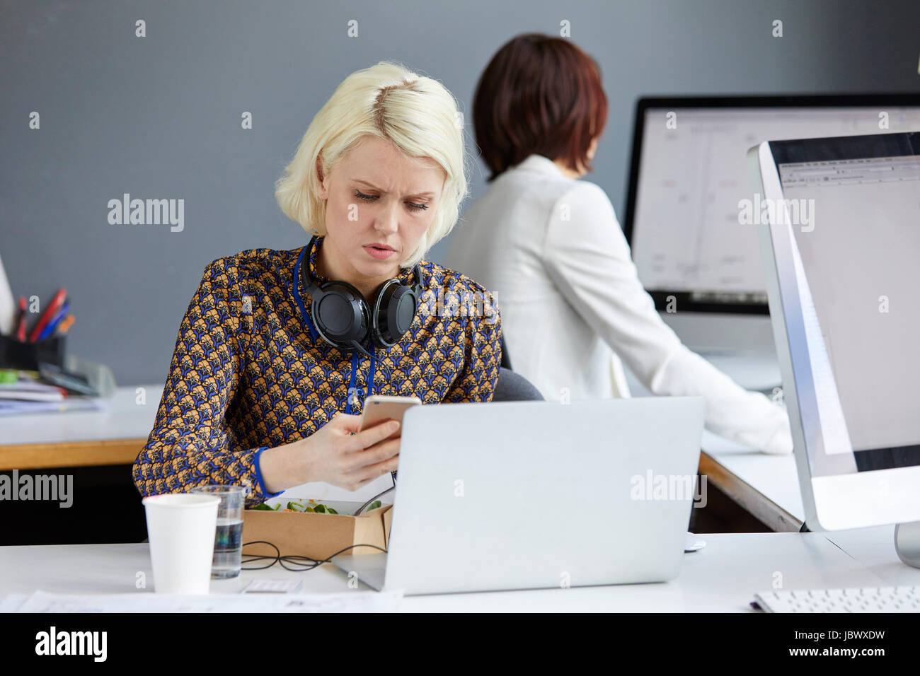 Designer femmina guardando smartphone durante un pranzo di lavoro alla scrivania in ufficio Foto Stock