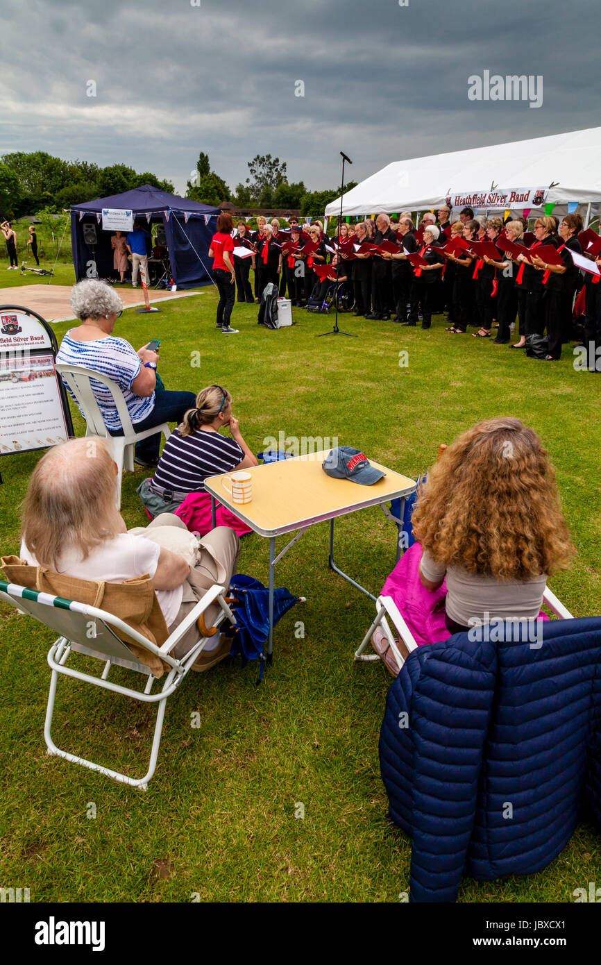 La popolazione locale guarda una comunità coro cantando sotto la pioggia a Maresfield Fete, Maresfield, East Sussex, Regno Unito Foto Stock