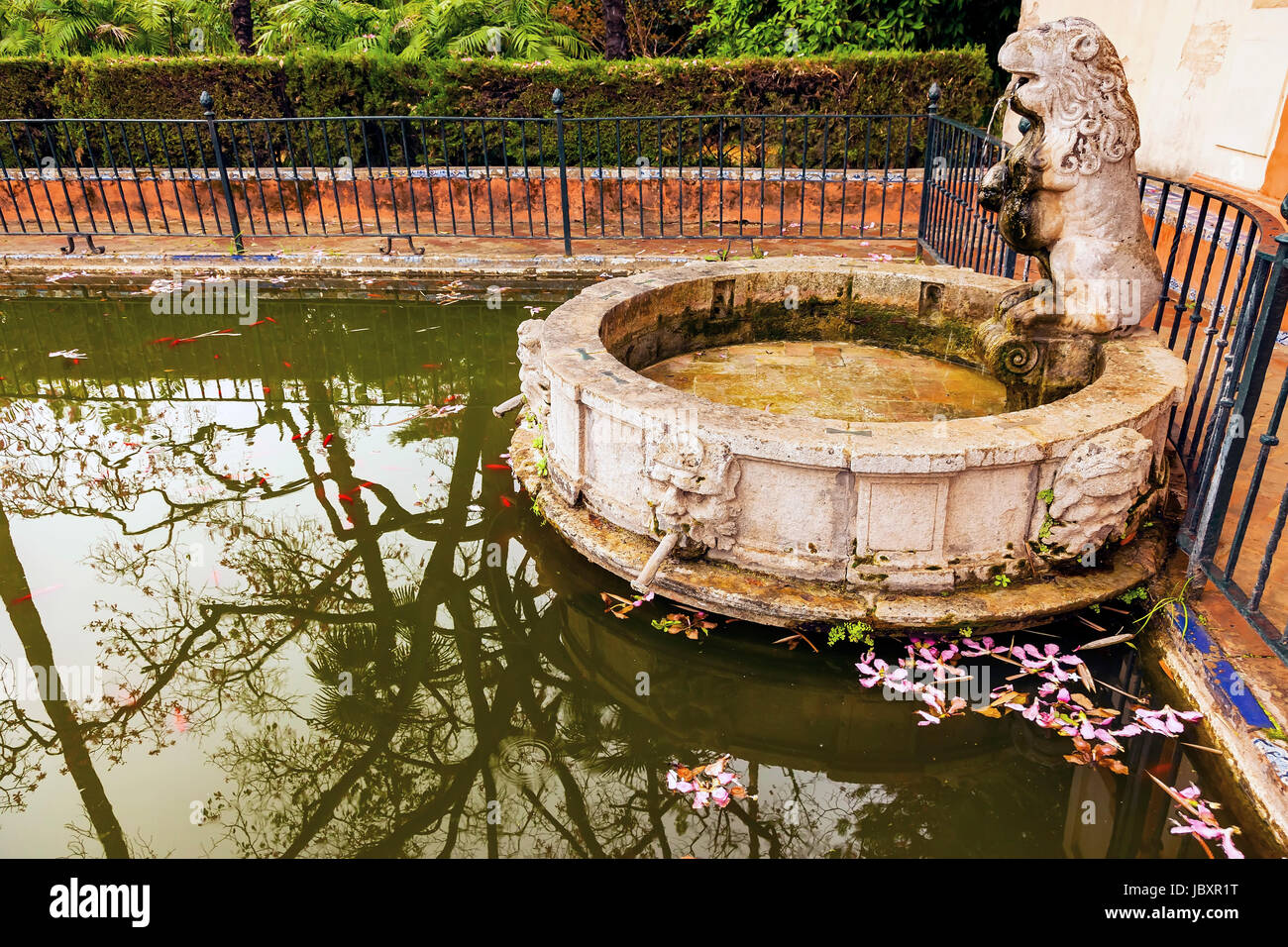 Lion Statua fontana riflessione piscina pesce giardino di fiori di Alcazar Royal Palace Siviglia Andalusia Spagna. Originariamente una fortezza moresca, più antico Palazzo Reale ancora in uso in Europa. Costruito nel 1100 e ricostruita nel 1300s. Foto Stock