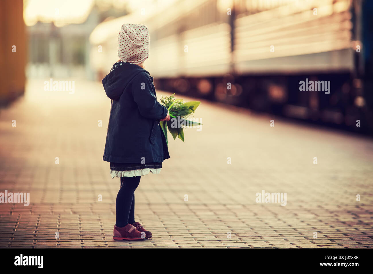 Bambina guarda che arrivano con il treno. Il capretto con fiori sulla piattaforma ferroviaria. Foto Stock