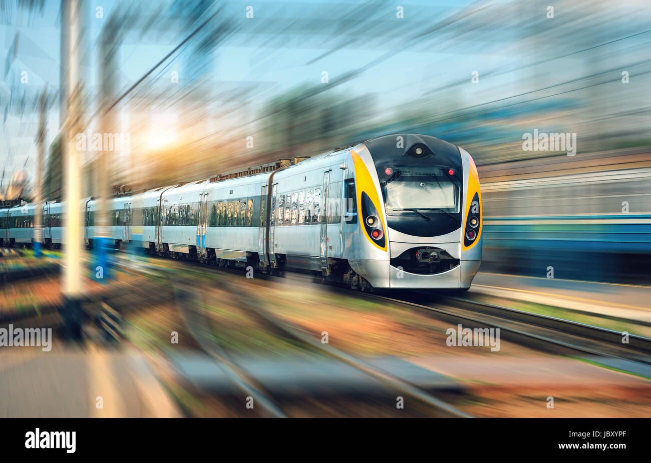 Treno ad alta velocità in movimento con la stazione ferroviaria al tramonto. Europeo moderno treno intercity sulla piattaforma ferroviaria con motion blur effetto. Industri Foto Stock