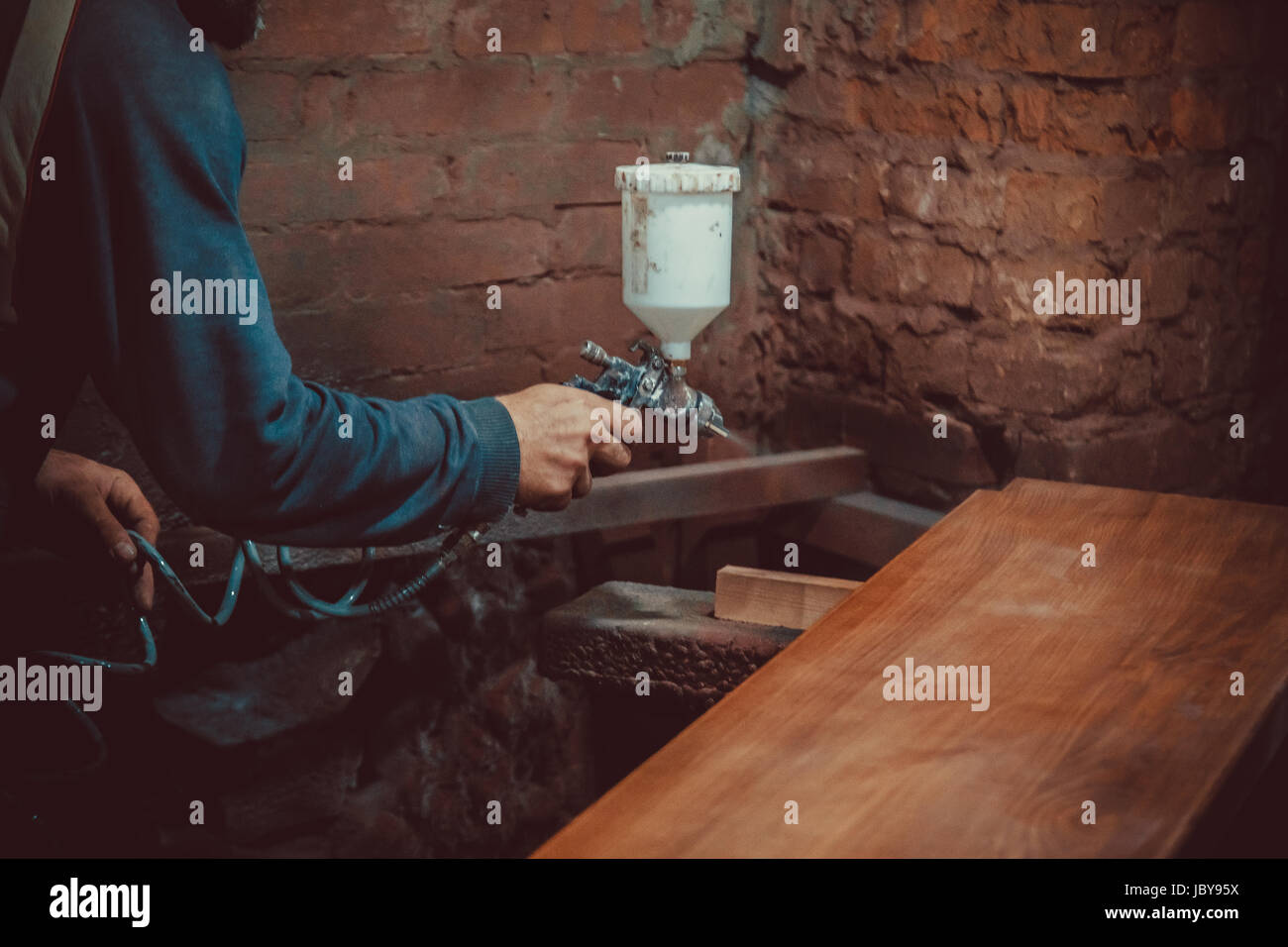 Il pittore in una fabbrica - Verniciatura industriale del legno con la pistola a spruzzo. soft focus. shallow dof. Foto Stock