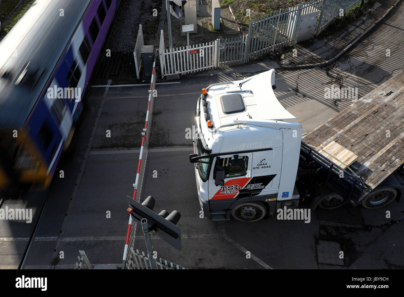 Mercedes-Benz Actros carrello tirando un vuoto rimorchio flatbed attende un treno per passare su un passaggio a livello a Rotherham, South Yorkshire Foto Stock