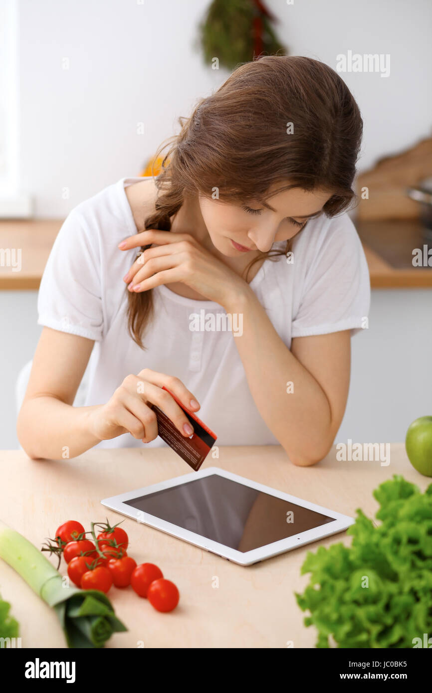 Giovane donna in cerca di una nuova ricetta per una cottura in cucina. La  casalinga è rendere lo shopping online dal computer tablet e carta di  credito Foto stock - Alamy