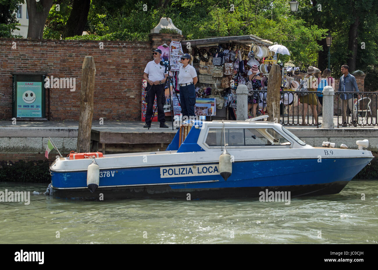 Venezia, Italia - 13 giugno 2017: due funzionari di polizia operante una trappola di velocità accanto a un occupato bancarella vendendo souvenir turistici sul Canal Grande di Venezia. Foto Stock
