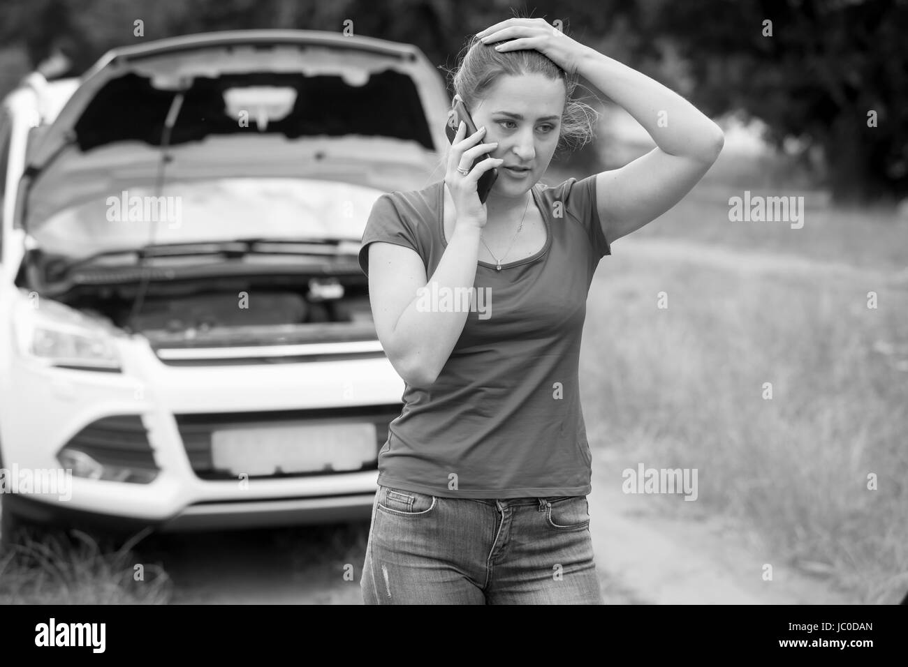 Ritratto in bianco e nero di sad woman standing a Broken auto e chiede aiuto Foto Stock