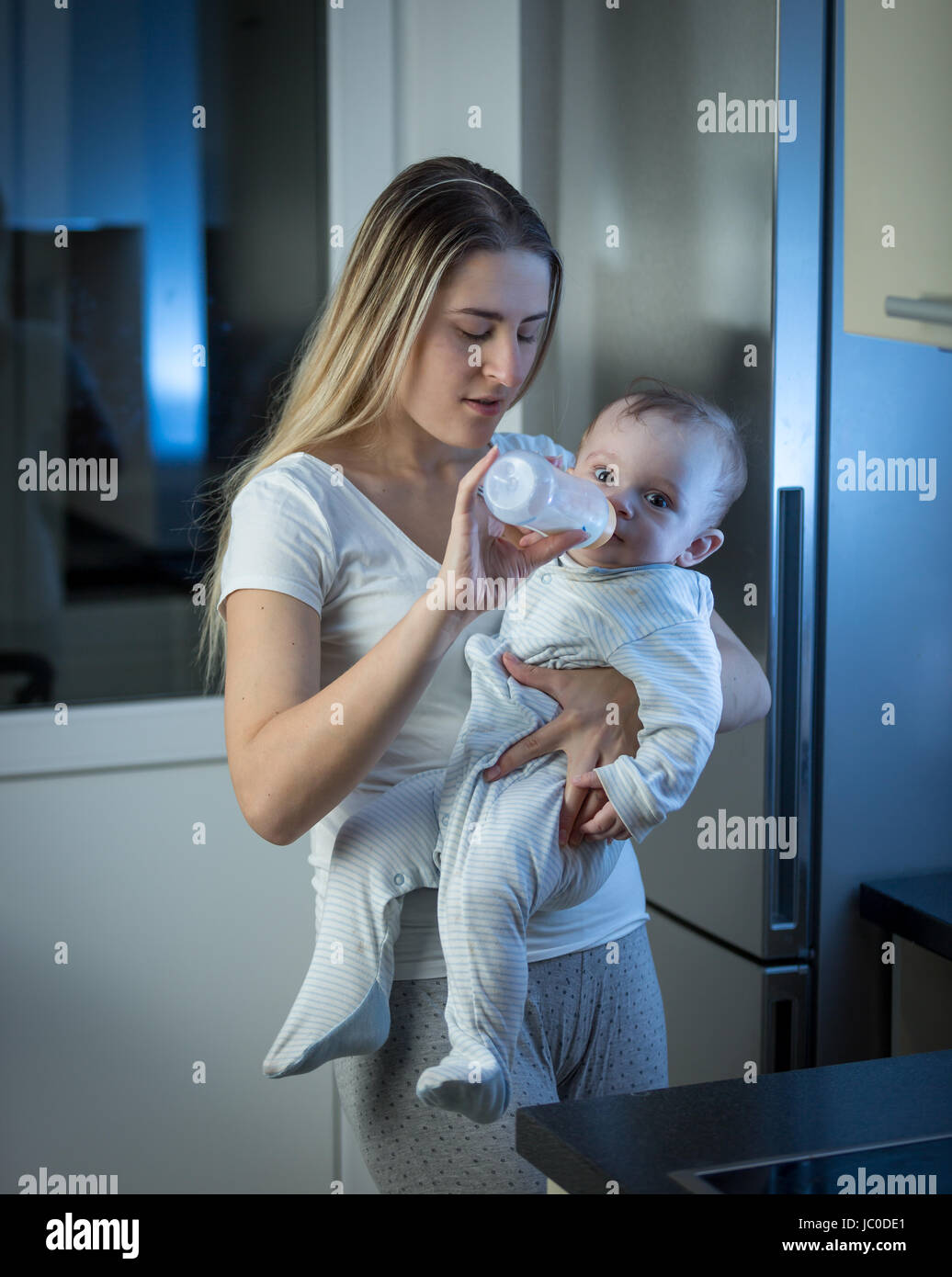 Ritratto di giovane madre dando figlio bambino il latte dalla bottiglia su cucina a mezzanotte Foto Stock