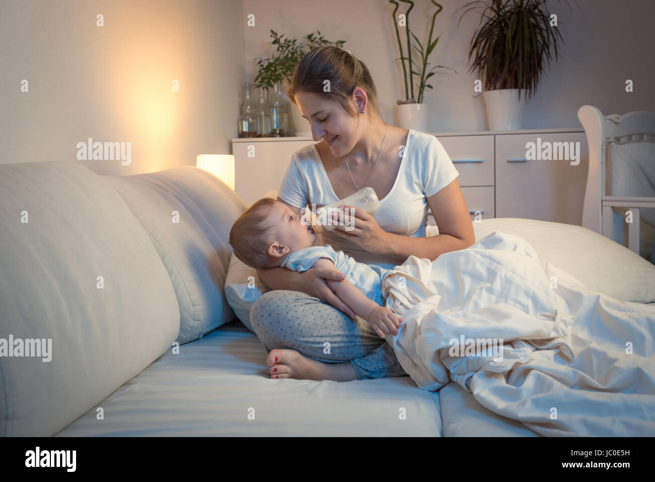 Ritratto di giovane madre che nutre il suo bambino dal flacone nel letto di notte Foto Stock