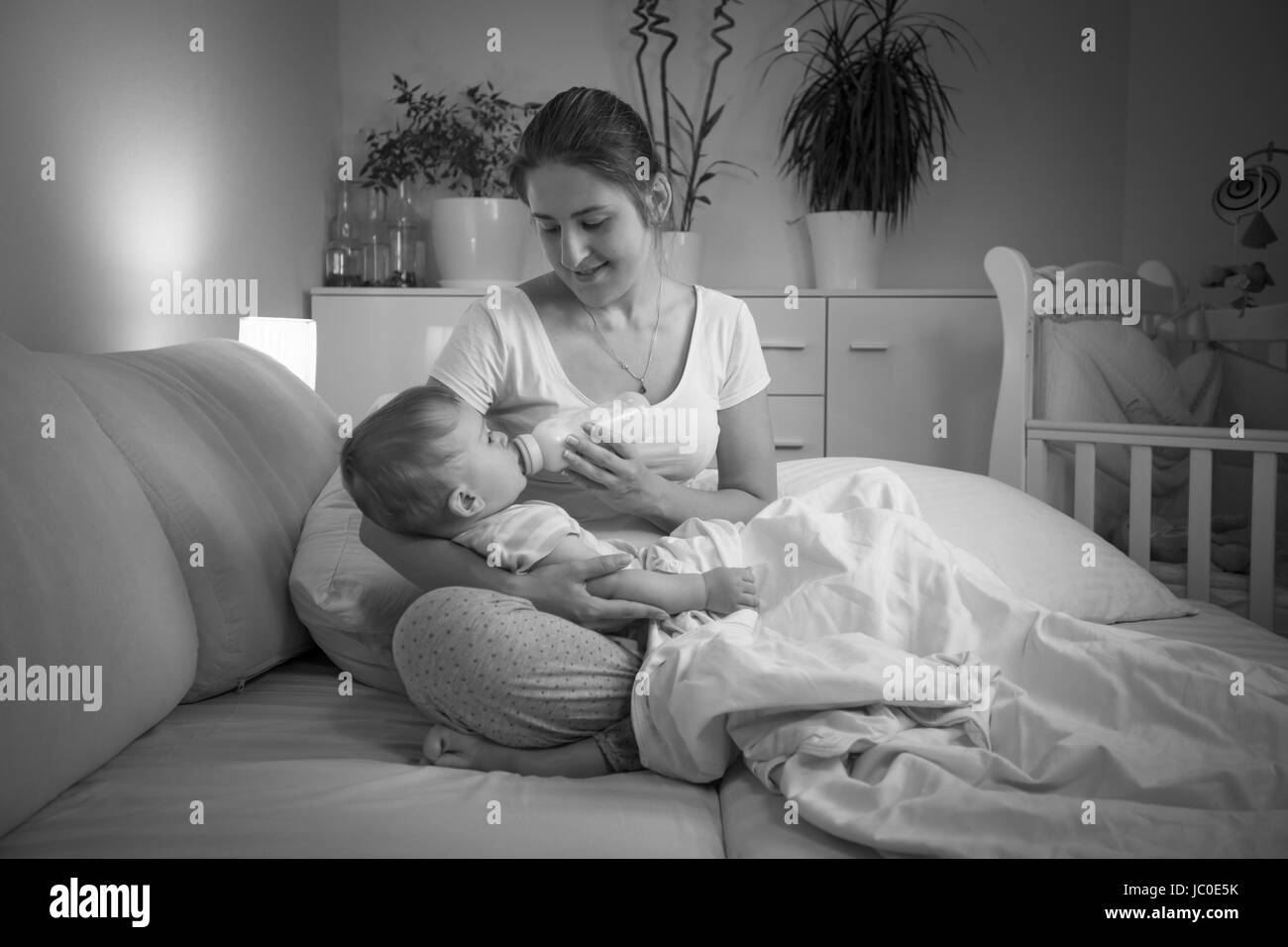 Bianco e nero ritratto di giovane madre che nutre il suo bambino a notte da bottiglia Foto Stock