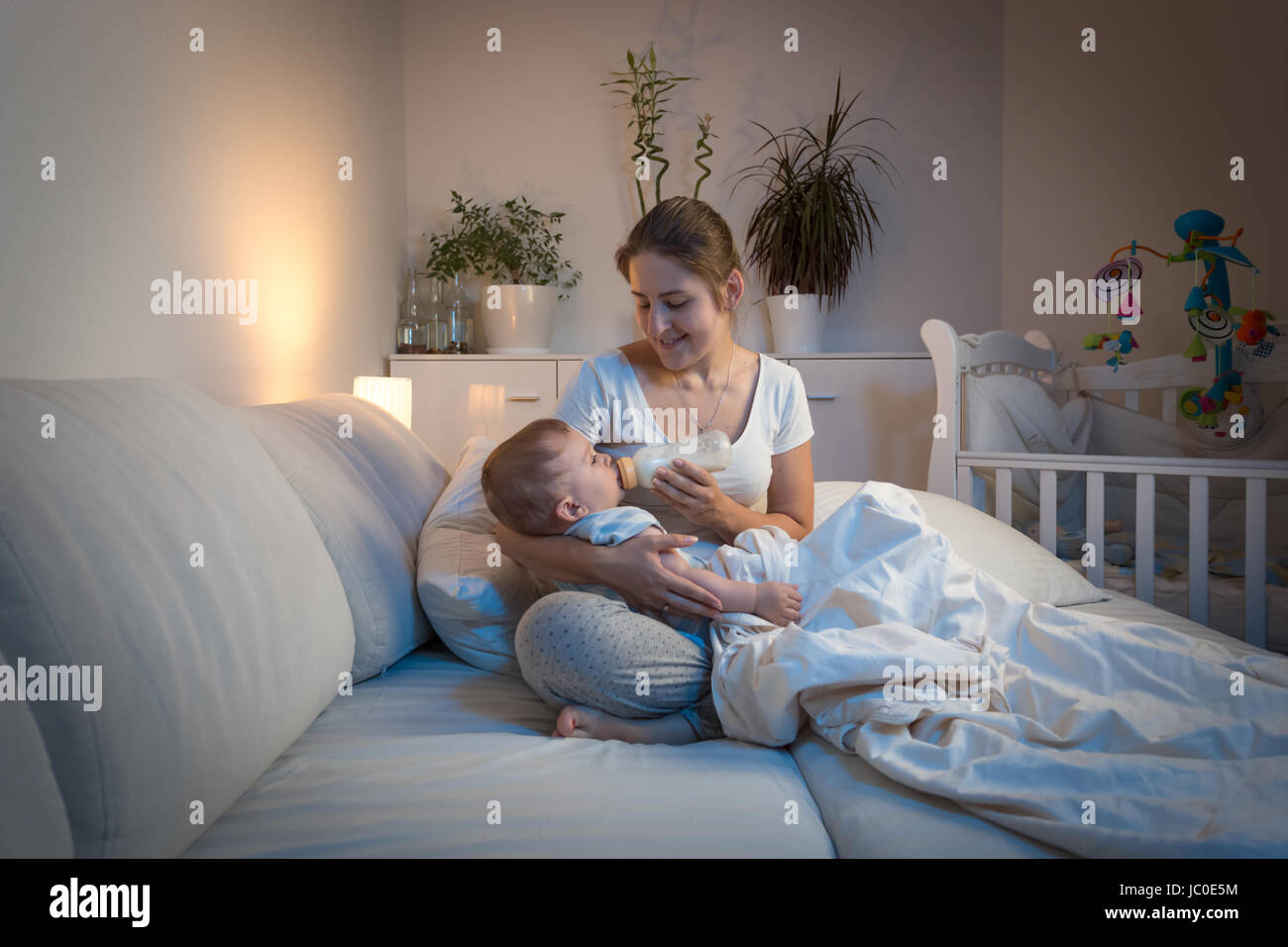 Ritratto di giovane e bella madre di dare il latte al suo bambino nel letto di notte Foto Stock
