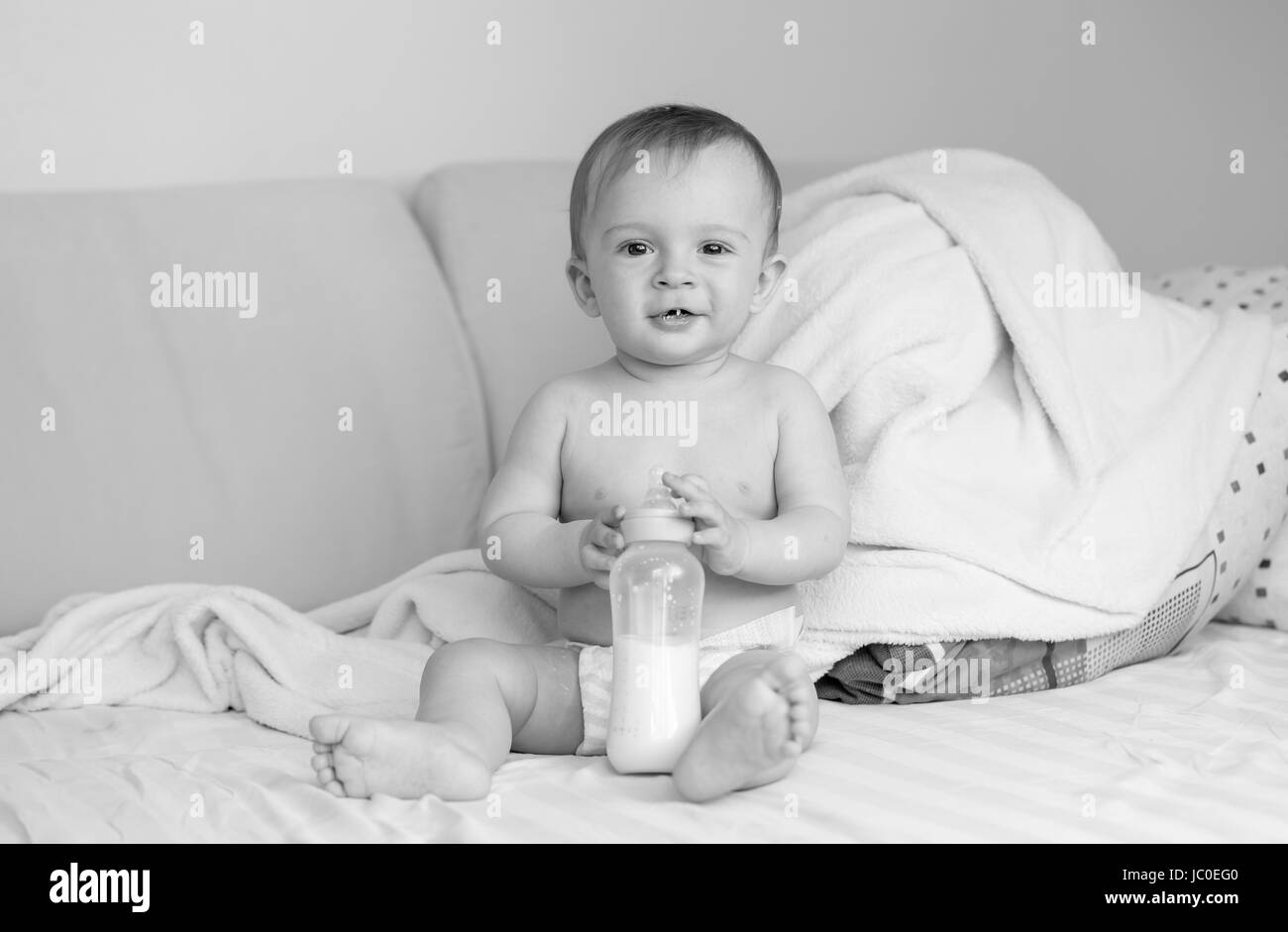 Foto in bianco e nero del simpatico bimbo seduto sul letto con bottiglia di latte Foto Stock