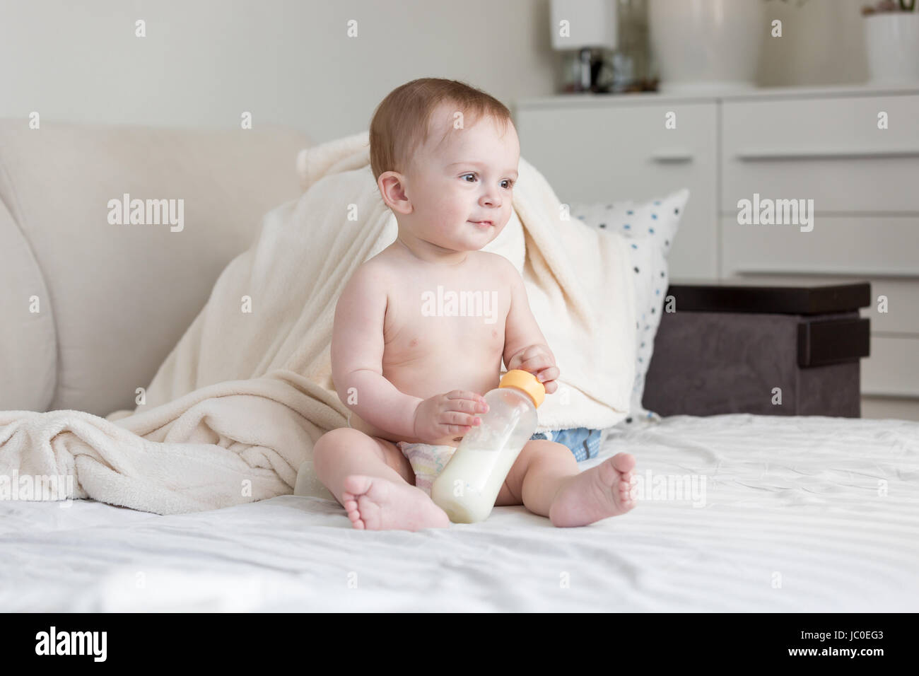 Bella carino baby in pannolini seduta sul letto con bottiglia di latte Foto Stock