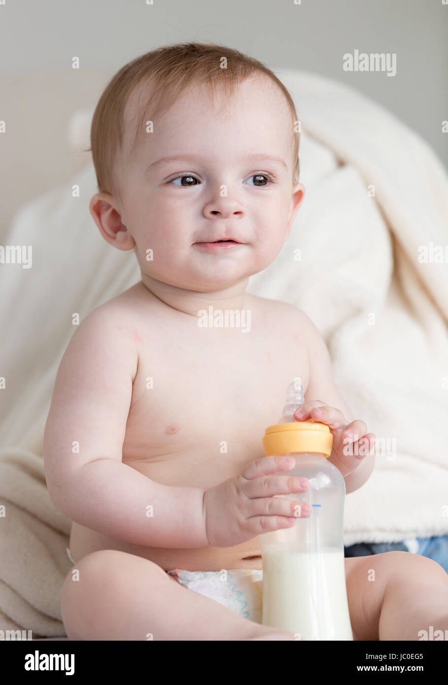 Adorabili di 9 mesi baby boy in pannolini seduti sul divano e tenendo la bottiglia con il latte Foto Stock