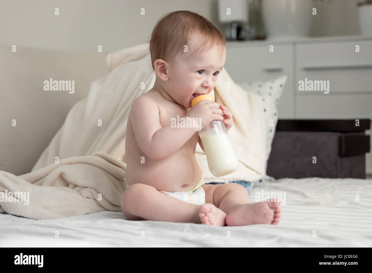 Bella 9 mesi di età bambino seduto sul letto e bere latte dalla bottiglia Foto Stock