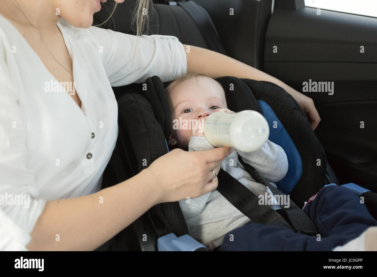 Ritratto di piccolo bimbo a bere il latte dal biberon sulla vettura del sedile posteriore Foto Stock