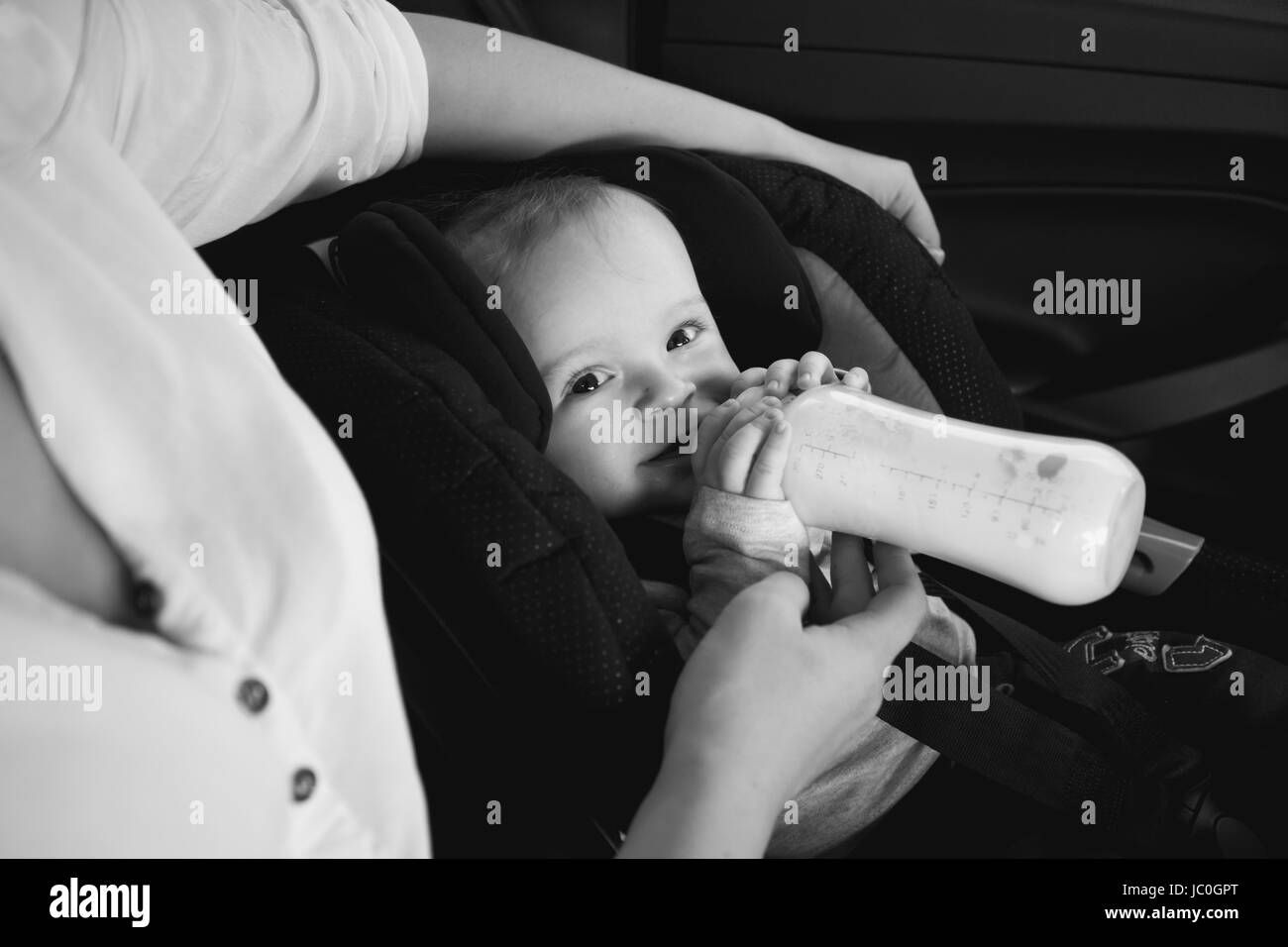 Bianco e nero ritratto della madre del bambino di alimentazione dalla bottiglia in auto Foto Stock