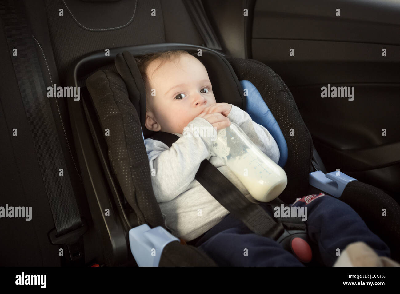 Ritratto di simpatici baby boy bere latte in auto seggiolino per bambini Foto Stock