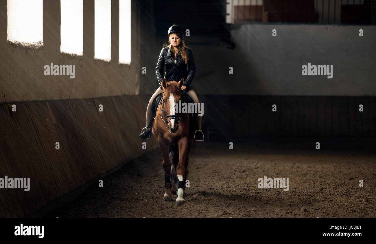 Foto orizzontale di donna di equitazione in maneggio in sala di equitazione Foto Stock