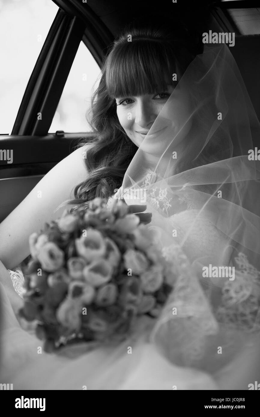 Ritratto monocromatico di sposa bella seduta in auto e bouquet di contenimento Foto Stock