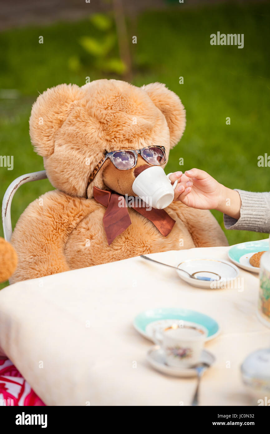 Primo piano della ragazza dando il tè di Teddy bear in occhiali da sole Foto Stock