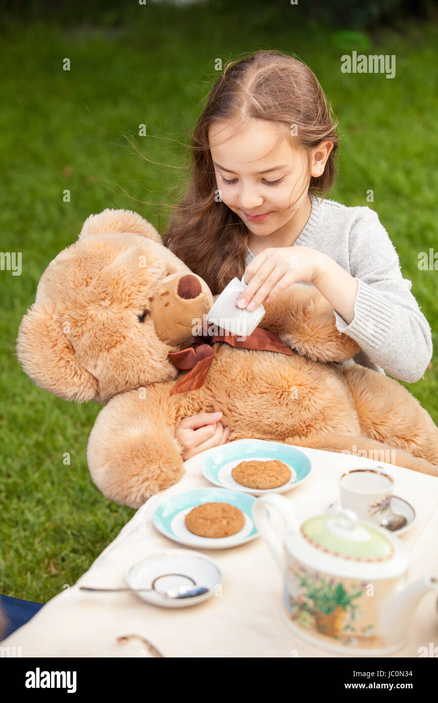 Bella ragazza sorridente dando il tè di orso di peluche Foto Stock