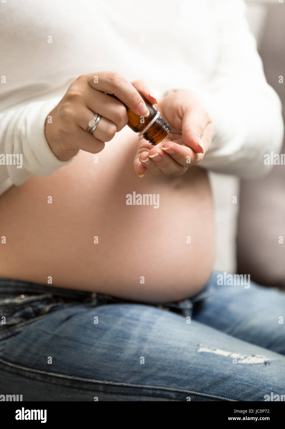 Primo piano della donna incinta assunzione di vitamine in pillole dalla bottiglia di vetro Foto Stock