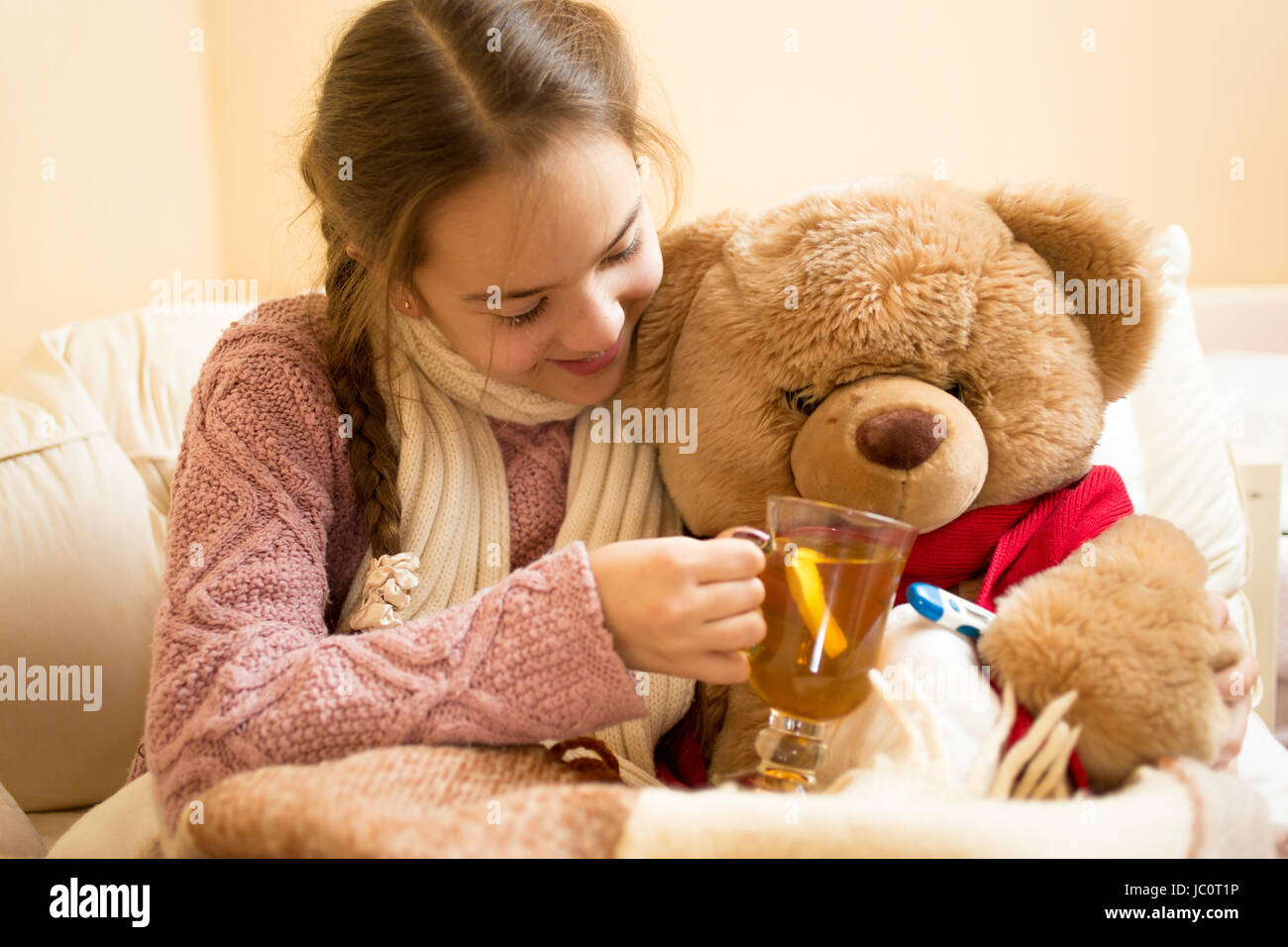 Primo piano della piccola ragazza malata dando il tè caldo a Teddy bear Foto Stock