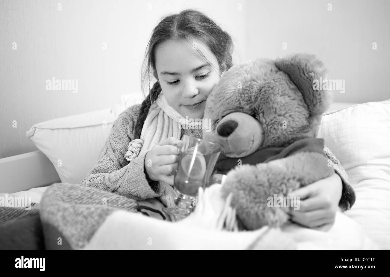 Bianco e nero ritratto di carino ragazza distesa a letto e dare pillole di Teddy bear Foto Stock