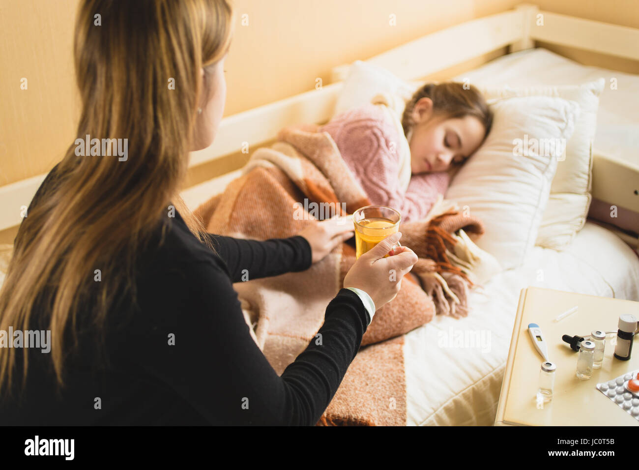 Giovane madre premurosa dando il tè caldo a figlia giacente a letto Foto Stock