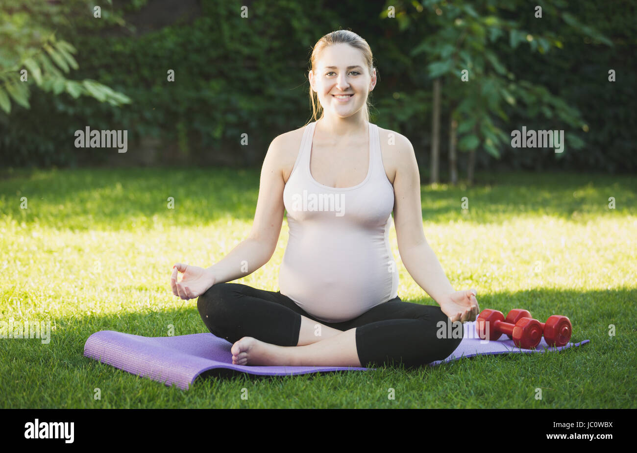 Bella donna incinta seduta in lotus pongono su erba a park Foto Stock