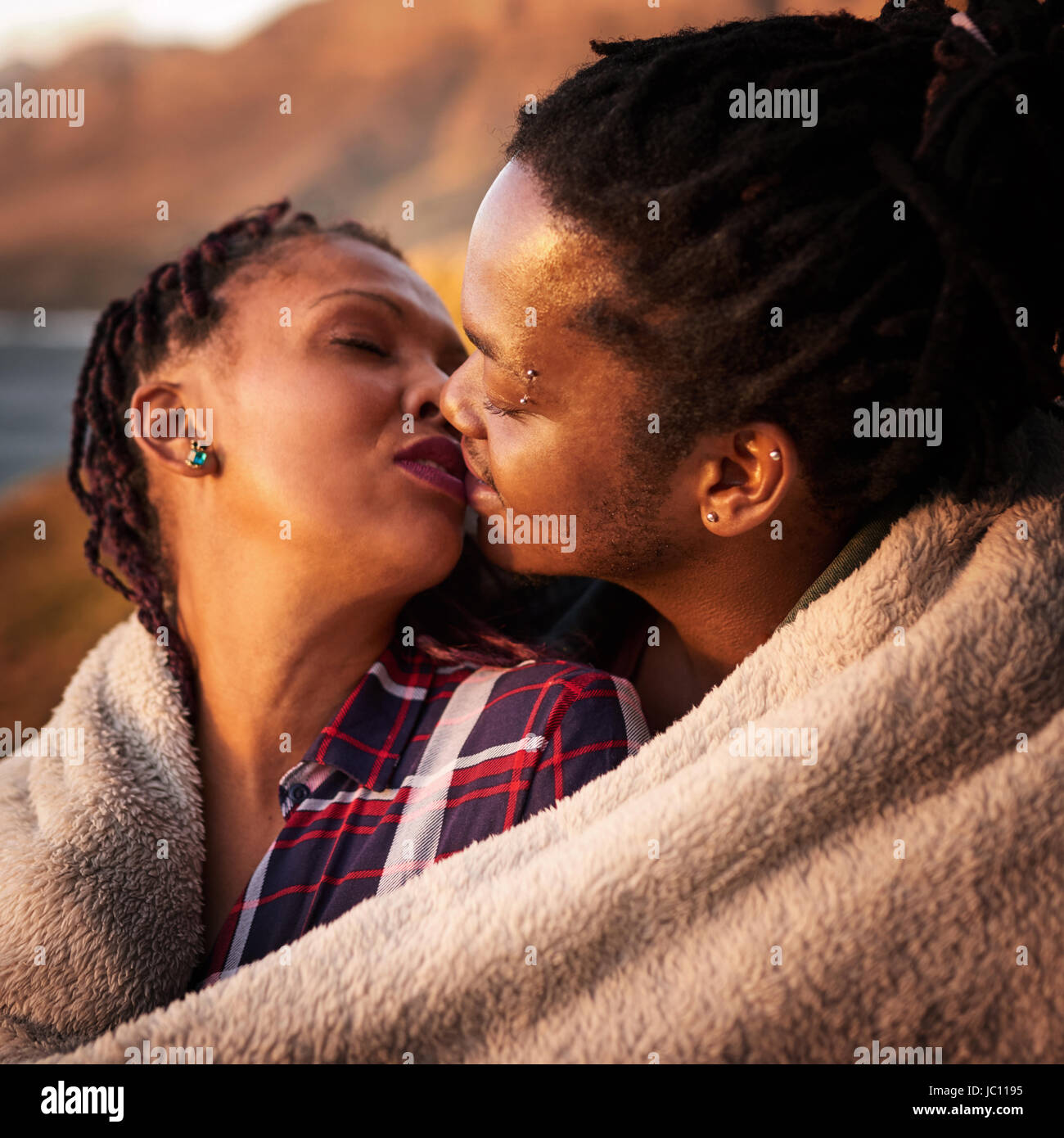 Close up razza mista giovane kissing all'aperto sotto una coperta Foto Stock