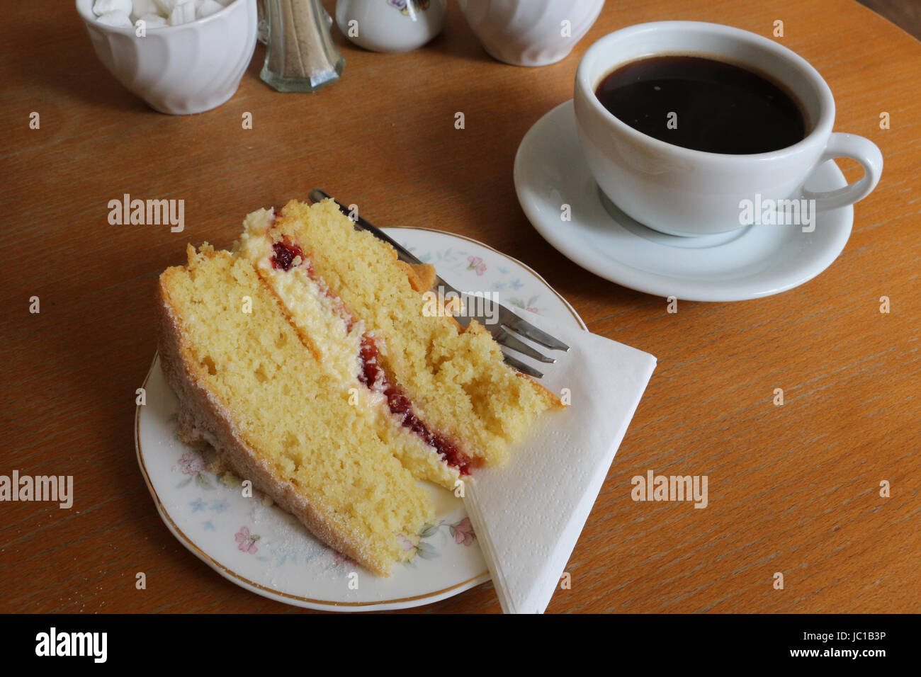 Fetta di una Victoria sponge cake (giallo torta con marmellata e glassa) e  una tazza di caffè in porcellana bianca contro un tavolo marrone per una  pausa mattutina Foto stock - Alamy