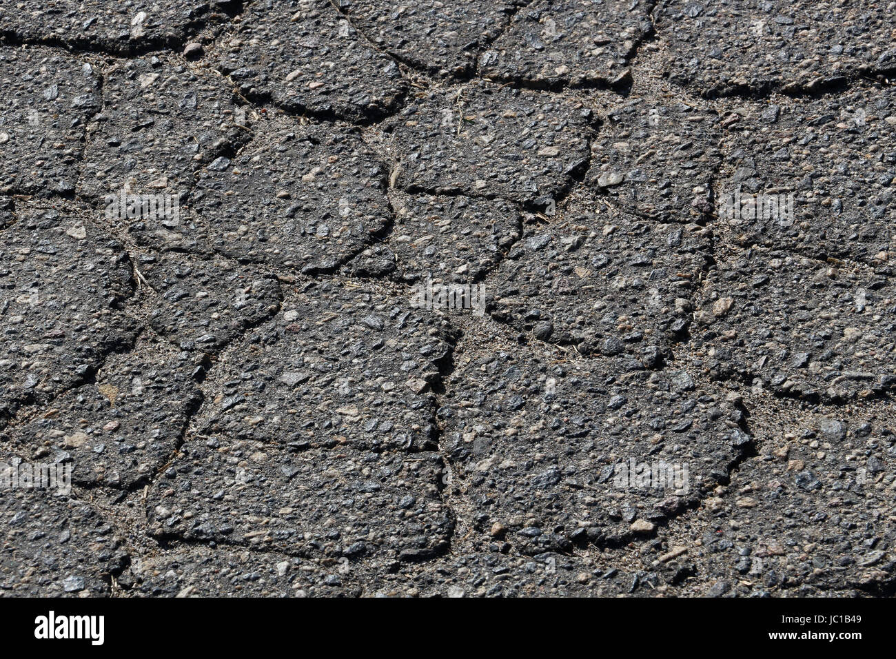 Sgretolamento di asfalto nero massicciata cracking in una configurazione reticolare, con presenti macchie di ghiaia. Tenuto male strada asfaltata. Necessita di manutenzione. Foto Stock