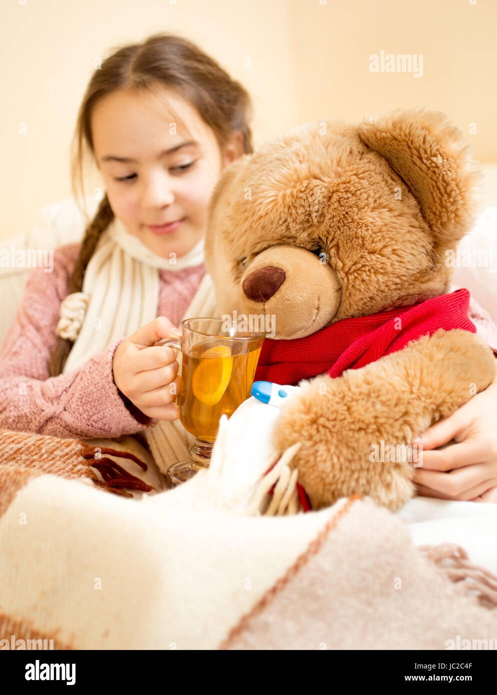 Primo piano della ragazza malata che giace nel letto e dando il tè di Teddy bear Foto Stock