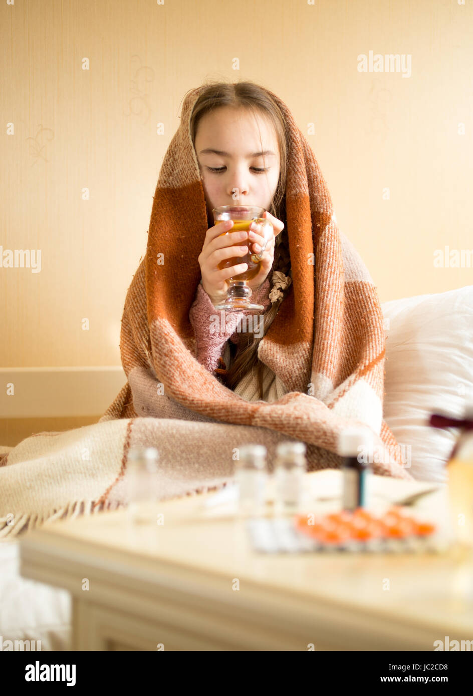 Ritratto di bambina coperte di plaid seduta sul letto e bere il tè Foto Stock