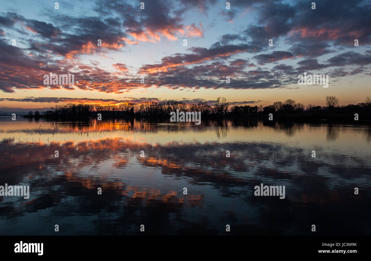 Perfettamente simmetrica riflessioni di alberi e cielo su un lago al tramonto Foto Stock