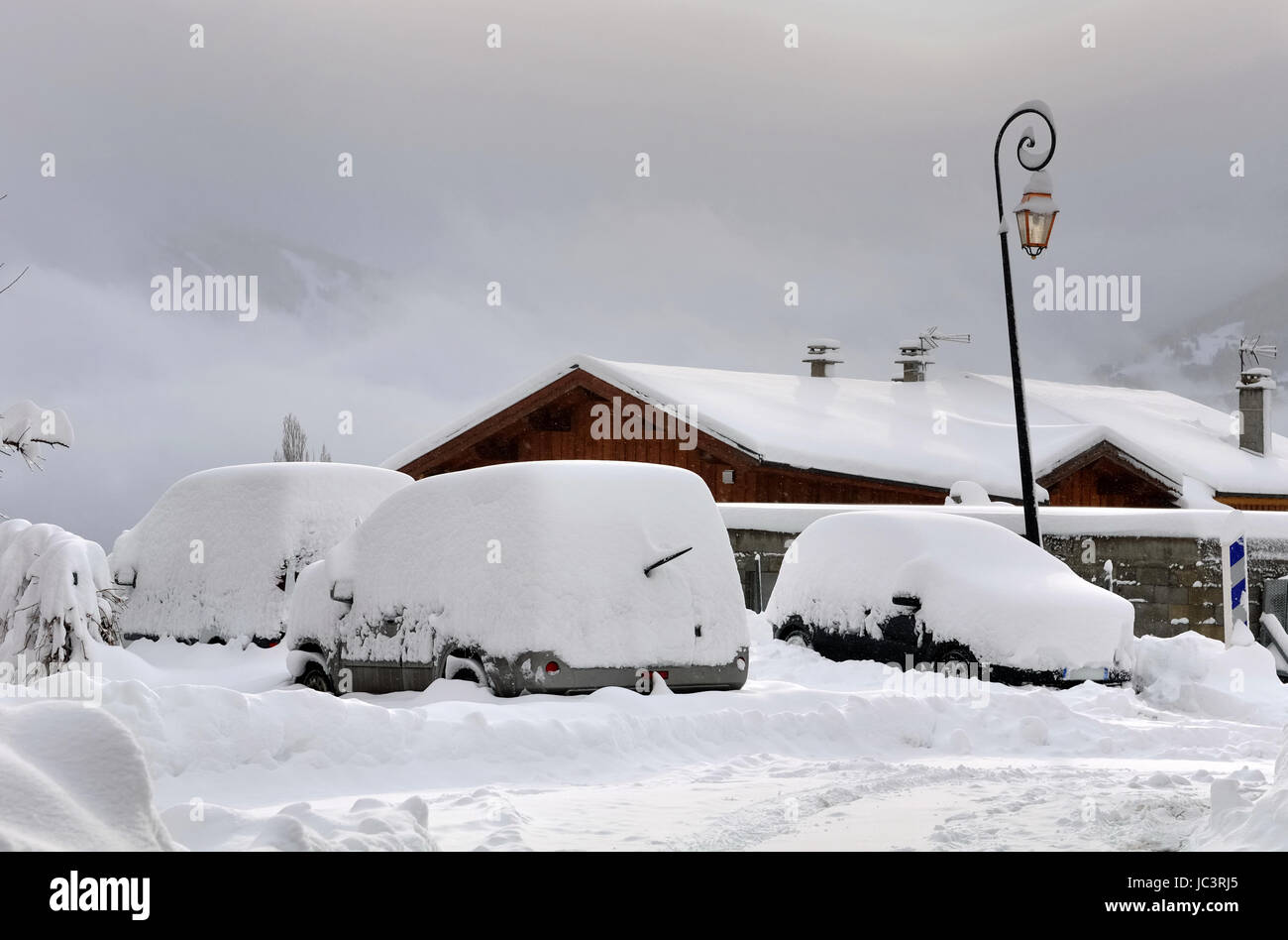 Snowy auto in un parcheggio in un villaggio di montagna Foto Stock