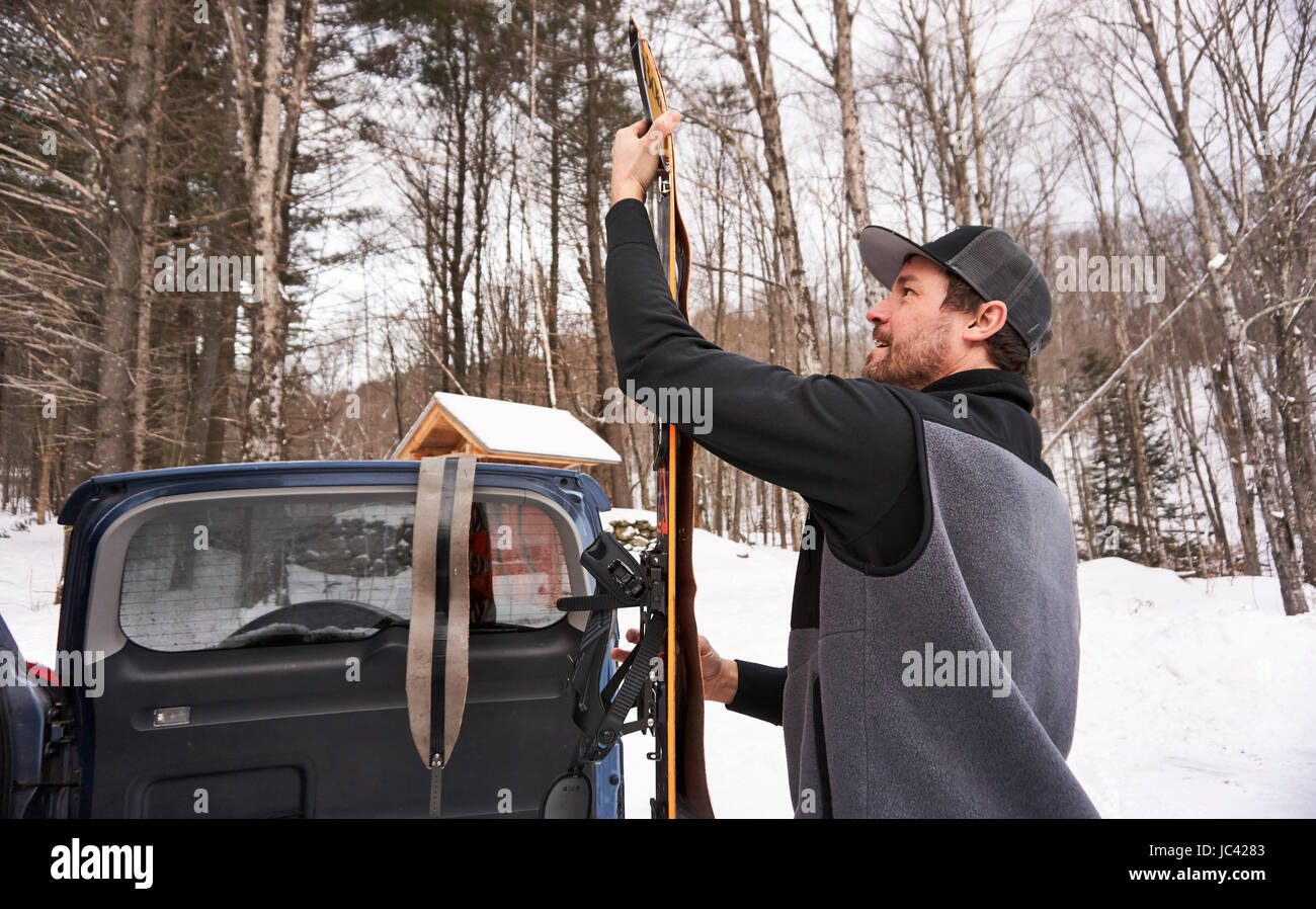 Un uomo applicando le pelli a sua splitboard nel parcheggio al sentiero. Foto Stock