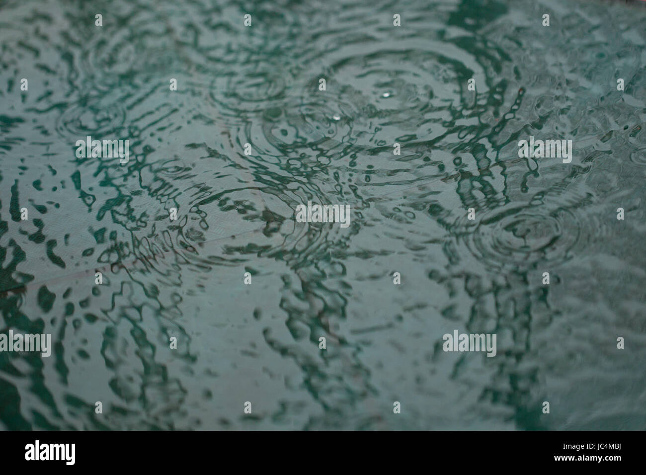 Caduta di pioggia increspature su una piccola piscina di acqua. Abstract, texture, sfondo. Sfuocata sui bordi per enfasi. Foto Stock