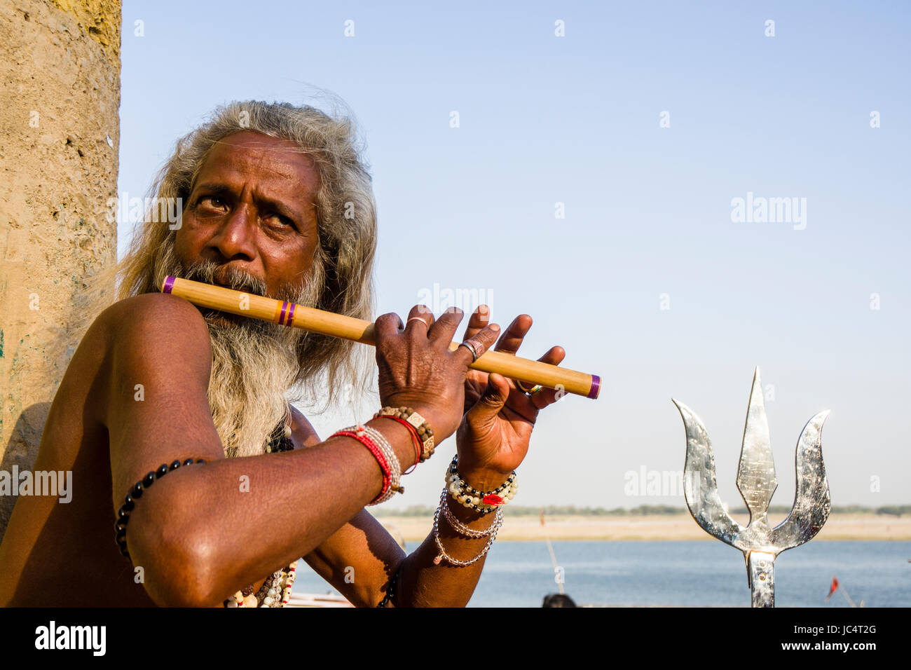 Un sadhu, uomo santo, è seduto e suonare il flauto su una piattaforma presso il fiume sacro Gange a dashashwamedh ghat, principale ghat, nel sobborgo godowlia Foto Stock