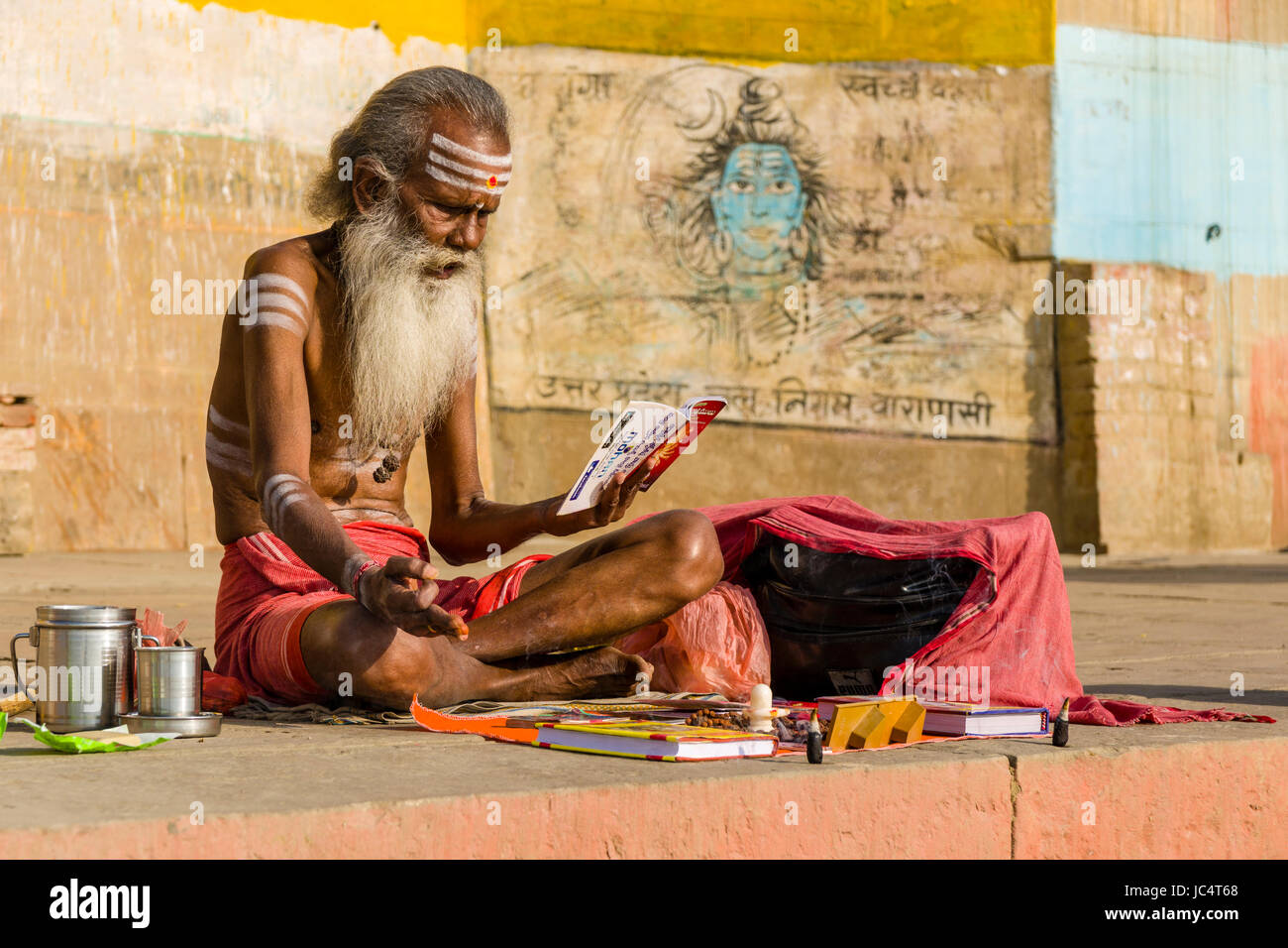Un sadhu, uomo santo, è seduto su una piattaforma e studiando skriptures religiosa presso il fiume sacro Gange a meer ghat nel sobborgo godowlia Foto Stock
