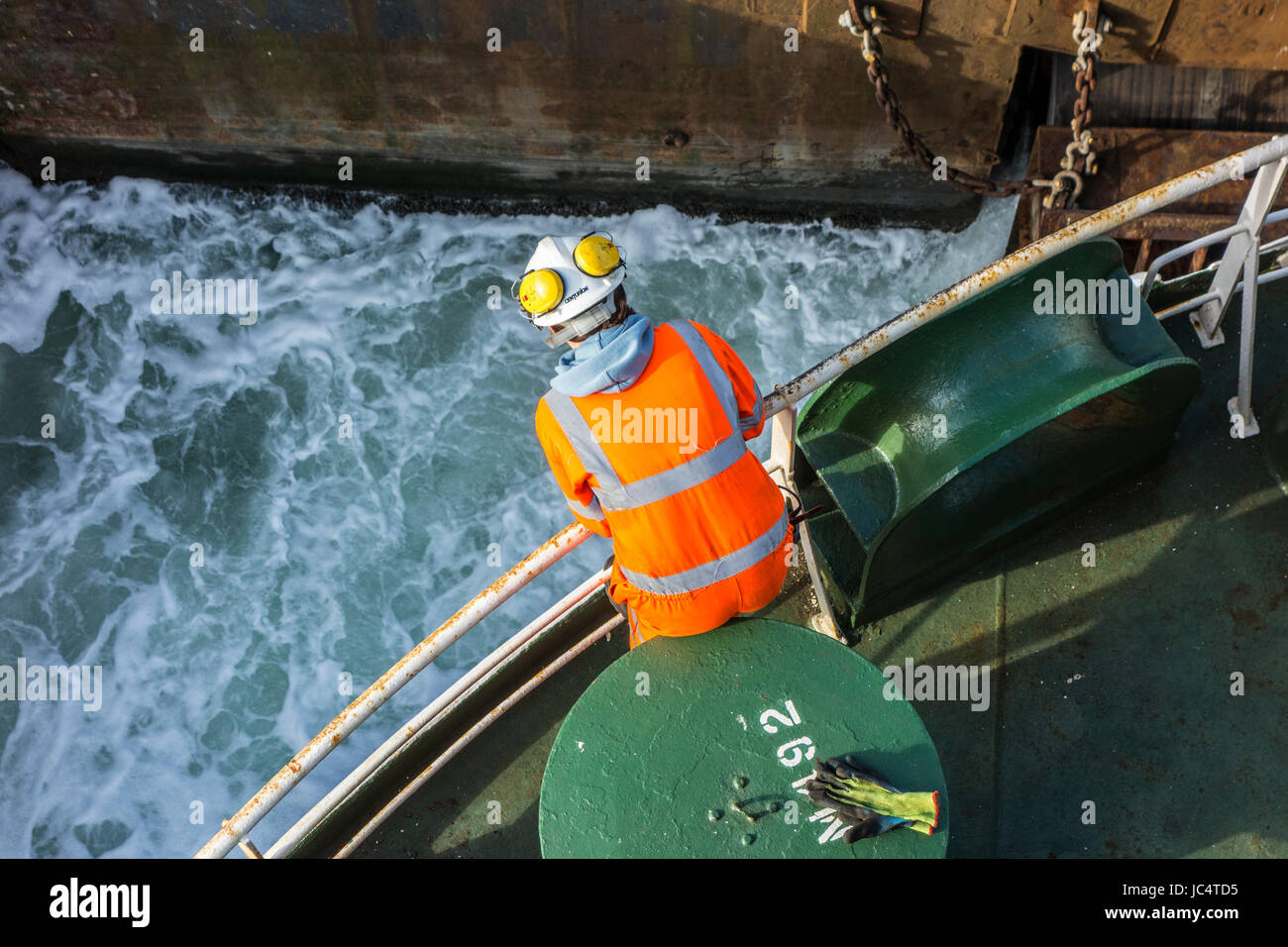Femmina membro di equipaggio in arancione in generale e di indossare il casco di sicurezza lavorando sul ponte di car carrier / nave da carico nel porto marittimo Foto Stock