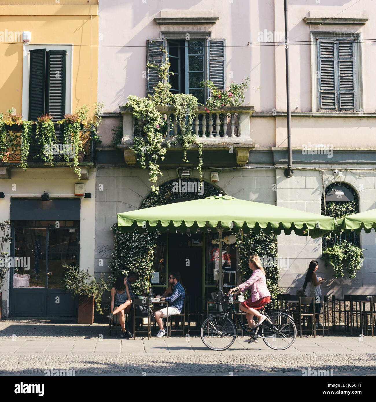 Milano cultura dei caffè con la donna che passa su una bicicletta su un giorno di estate Foto Stock