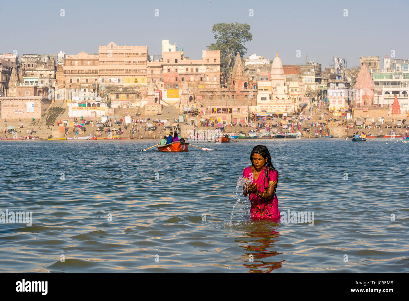 Una donna, pellegrino, sta facendo il bagno e pregando su banchi di sabbia di fiume santo Ganges, panorama di Dashashwamedh Ghat, principale Ghat, nella distanza Foto Stock