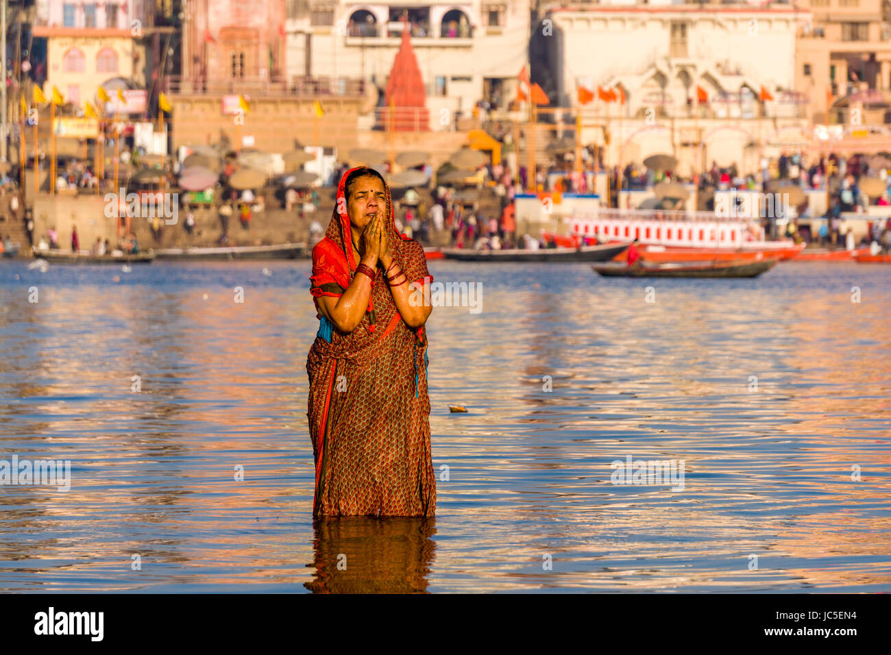 Una donna, pellegrino, sta facendo il bagno e pregando su banchi di sabbia di fiume santo Ganges, panorama di Dashashwamedh Ghat, principale Ghat, nella distanza Foto Stock