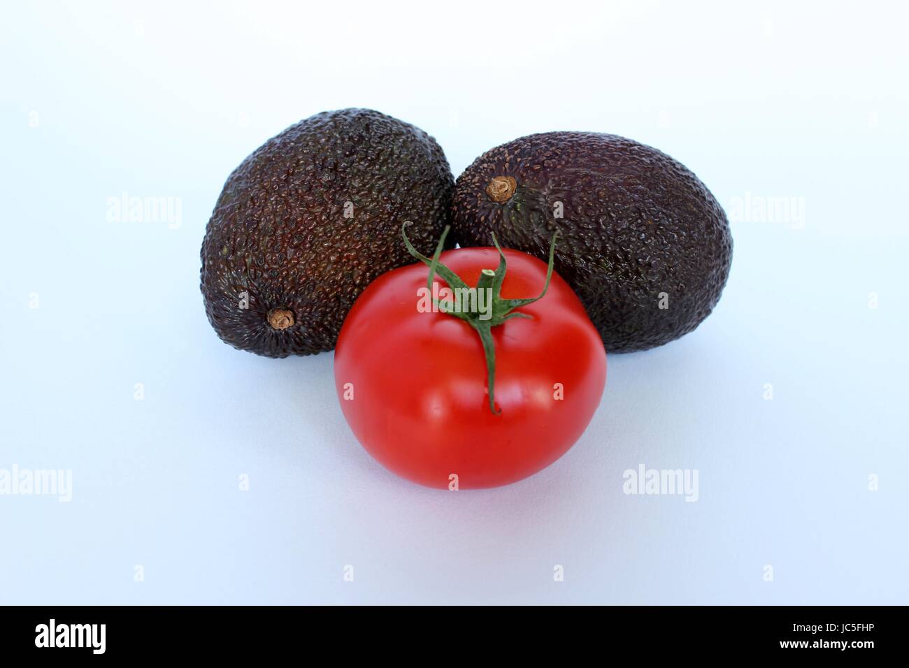 Un pomodoro accompagnato da una fresca avocado su sfondo bianco Foto Stock